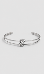 A silver-toned open cuff bangle bracelet featuring a textured rope-style band and a polished central knot detail, shown on a light gray background.