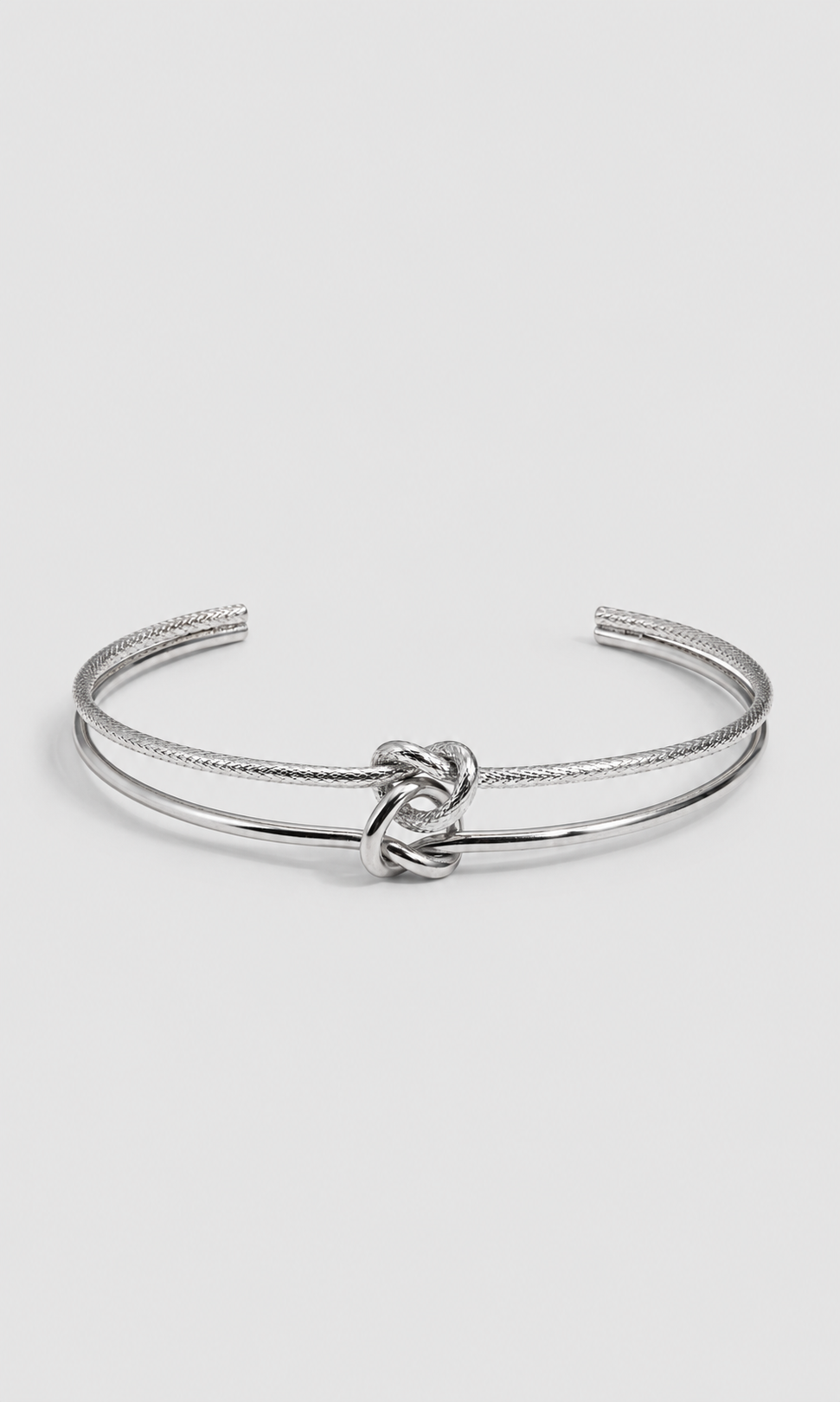 A silver-toned open cuff bangle bracelet featuring a textured rope-style band and a polished central knot detail, shown on a light gray background.