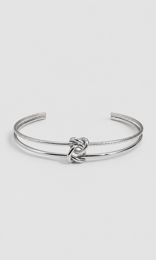 A silver-toned open cuff bangle bracelet featuring a textured rope-style band and a polished central knot detail, shown on a light gray background.