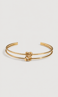 A gold-toned double-band cuff bracelet with a central knotted detail, shown on a light gray background.