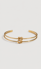 A gold-toned double-band cuff bracelet with a central knotted detail, shown on a light gray background.