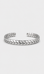 A silver-toned metal cuff bracelet with a textured, woven leaf-like pattern, displayed on a light gray background.