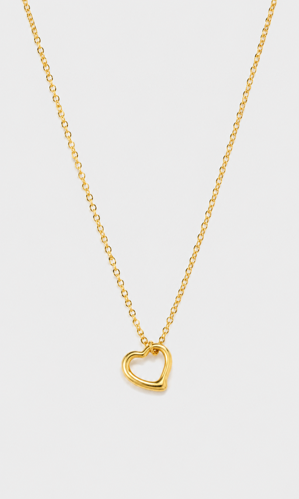 A delicate gold chain necklace featuring a small, polished open heart pendant, displayed against a clean, light gray background.
