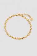 A gold chain bracelet with elongated oval links, a lobster clasp, and an extender chain with a round branded tag, photographed on a light gray background.