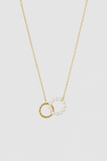 A delicate gold chain necklace featuring two interlocking circular pendants: one textured gold ring and one pearl-beaded gold ring, displayed against a solid light gray background.