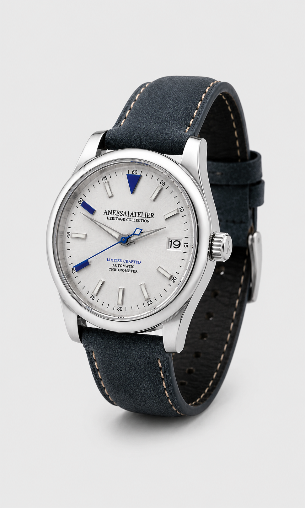 AneesaAtelier Automatic watch with a silver stainless steel case, white dial with blue accents, and a dark navy blue leather strap with tan contrast stitching, shown on a light gray background.