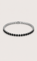A tennis-style bracelet with round black gemstones in a silver-toned setting, arranged in a circular shape on a light beige background.