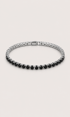 A tennis-style bracelet with round black gemstones in a silver-toned setting, arranged in a circular shape on a light beige background.