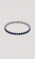 A tennis bracelet featuring rows of deep blue round-cut gemstones in a silver-toned setting, displayed on a neutral light gray background.