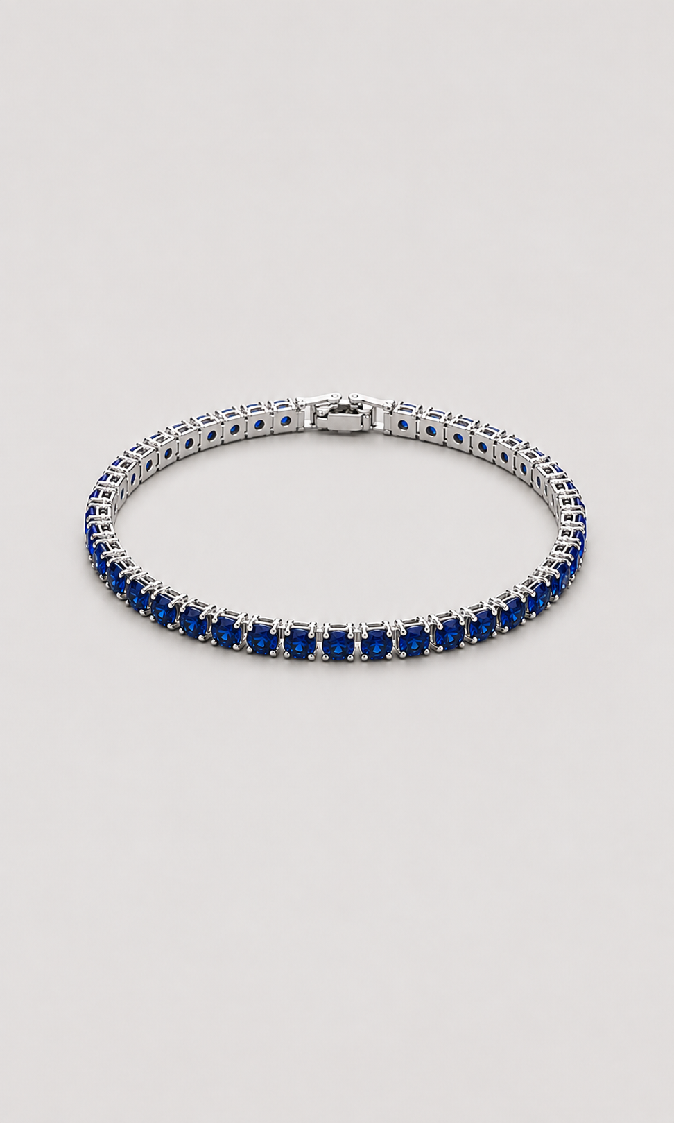 A tennis bracelet featuring rows of deep blue round-cut gemstones in a silver-toned setting, displayed on a neutral light gray background.