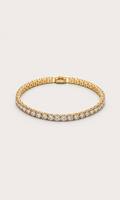 A gold tennis bracelet with a row of clear gemstones along the front, displayed on a light beige background.