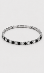 A tennis bracelet with alternating round black and clear stones in a silver-toned setting, shown against a light gray background.