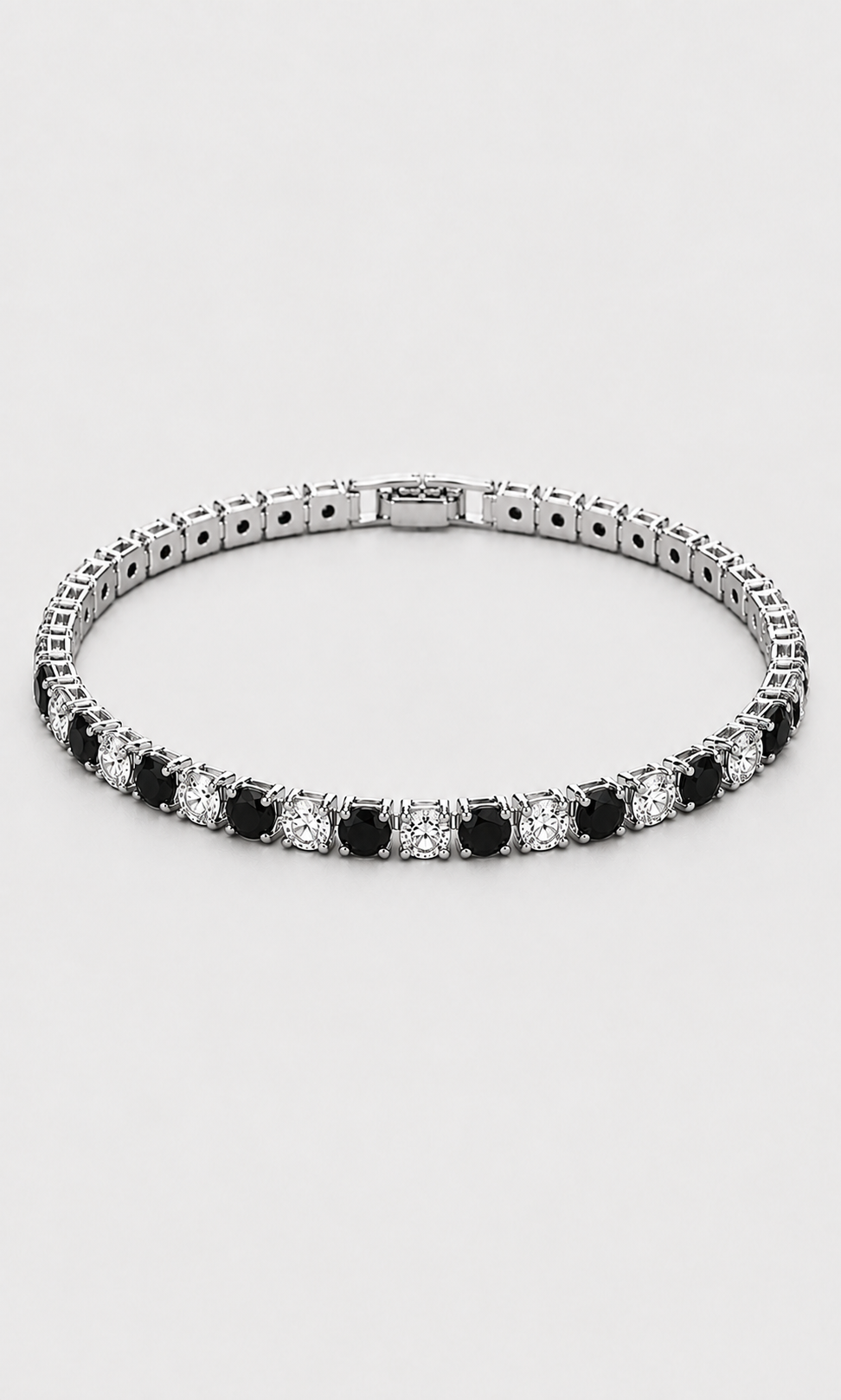 A tennis bracelet with alternating round black and clear stones in a silver-toned setting, shown against a light gray background.