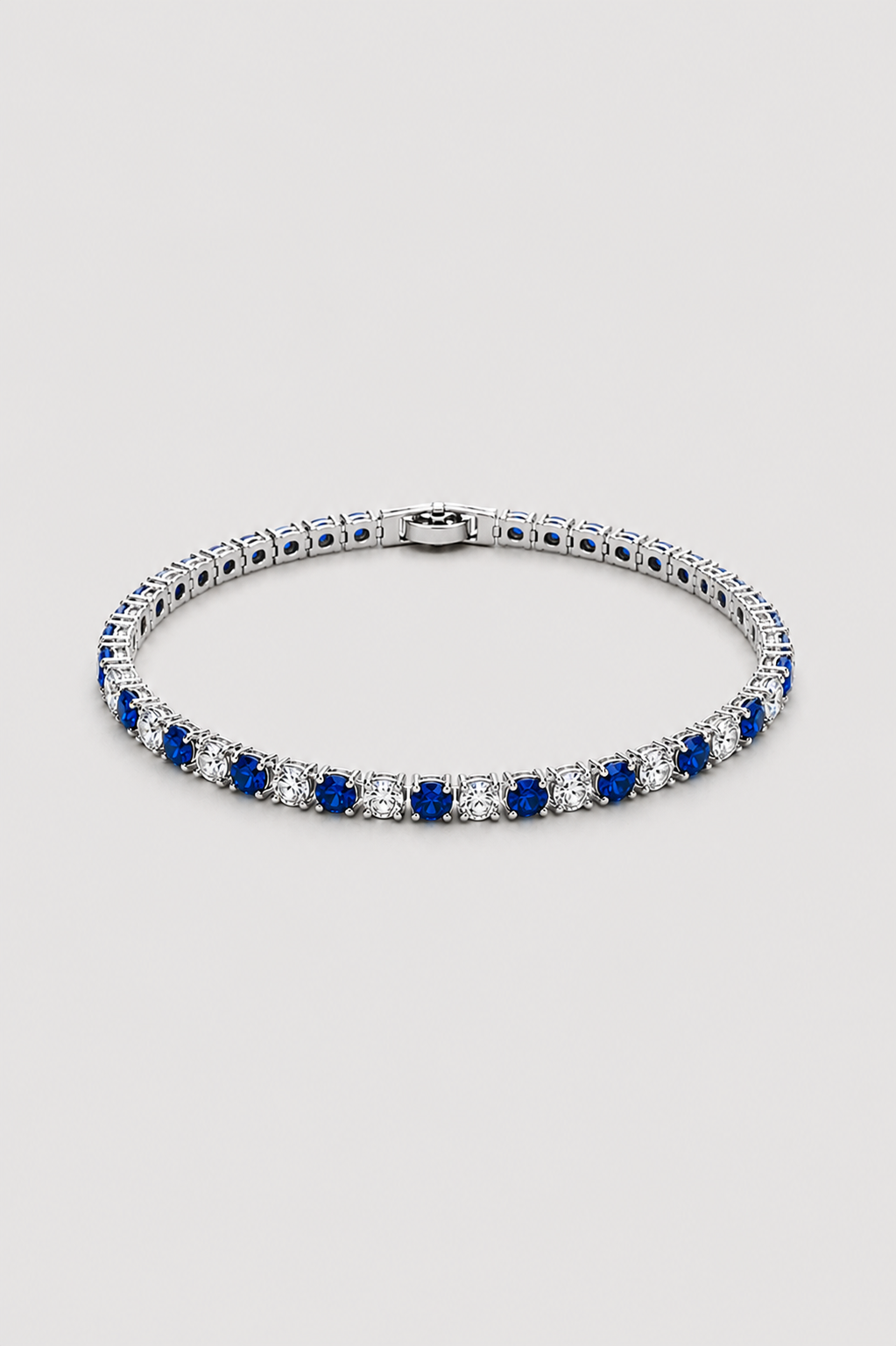 A tennis bracelet featuring alternating rows of deep blue sapphires and clear cubic zirconia stones in a silver-toned setting, displayed on a light gray background.