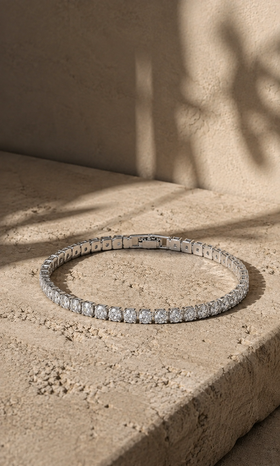 Silver tennis bracelet with sparkling stones, photographed on a warm beige natural stone surface in soft sunlight.