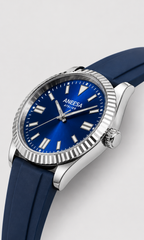 A close-up shot of an Aneesa ATELIER watch featuring a vibrant blue sunburst dial, silver-tone stainless steel case with a fluted bezel, and a dark blue silicone strap, set against a neutral light gray background.