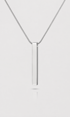 A silver vertical bar pendant necklace on a delicate silver chain, centered against a light gray background with a soft reflection below.