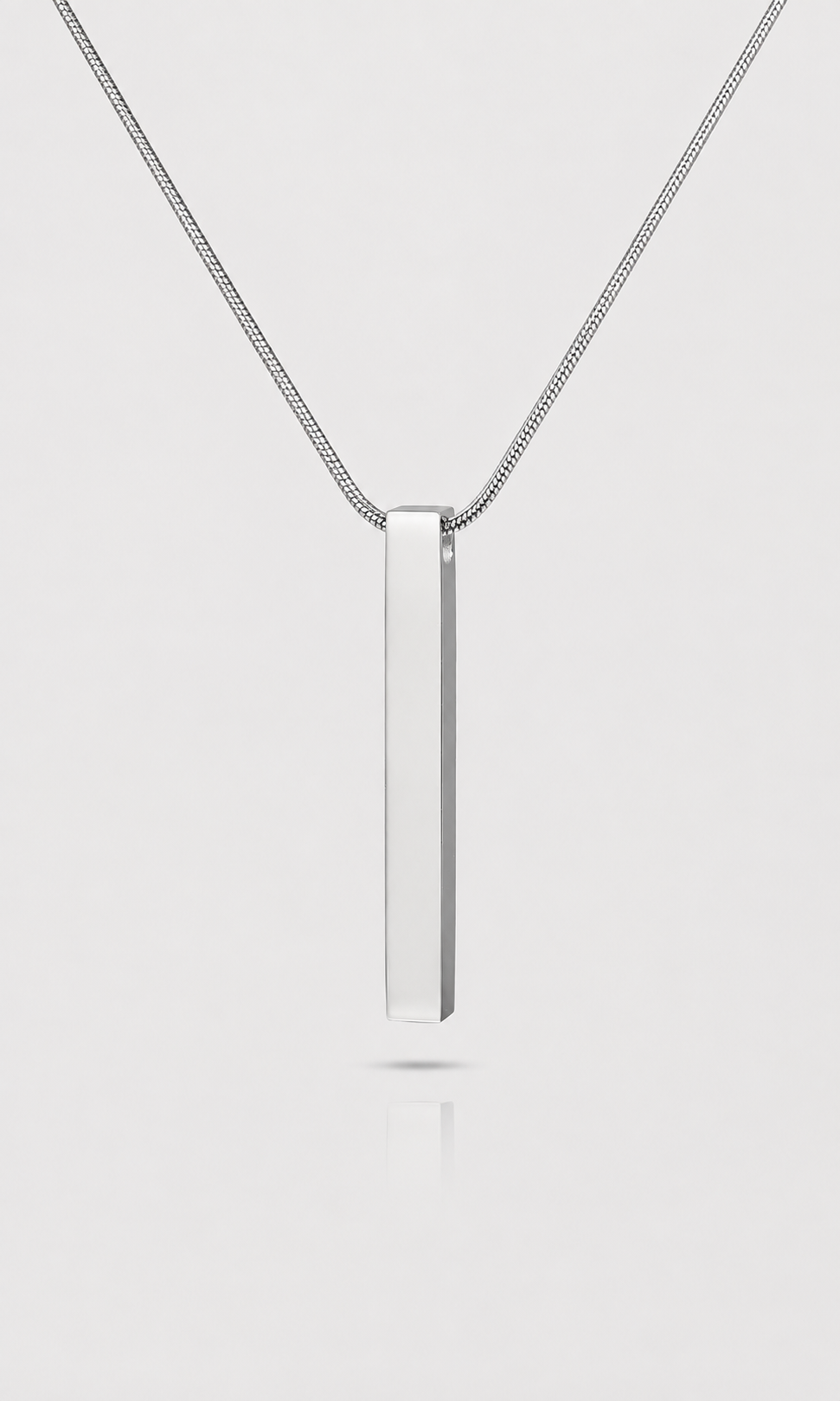 A silver vertical bar pendant necklace on a delicate silver chain, centered against a light gray background with a soft reflection below.
