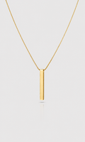 A minimalist gold necklace featuring a flat, polished vertical bar pendant on a delicate gold chain, presented against a light gray background.