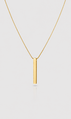 A minimalist gold necklace featuring a flat, polished vertical bar pendant on a delicate gold chain, presented against a light gray background.