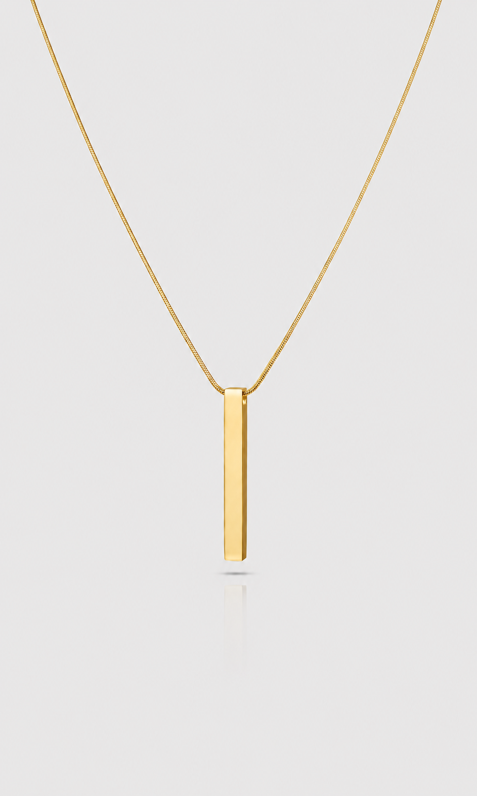 A minimalist gold necklace featuring a flat, polished vertical bar pendant on a delicate gold chain, presented against a light gray background.