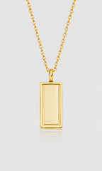 A gold rectangular pendant necklace with a smooth, polished finish, suspended from a matching gold chain against a light gray background.