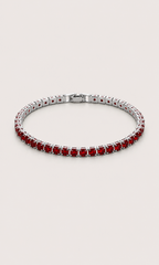 A silver tennis bracelet featuring round-cut red gemstones, displayed on a light beige background.