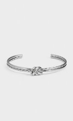 A silver-toned metal cuff bracelet featuring a central knotted detail and textured twisted edges, displayed on a clean, light gray background.