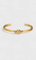 A gold-toned metal cuff bracelet featuring a textured twisted design and a central knotted detail, displayed on a clean light gray background.