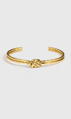 A gold-toned metal cuff bracelet featuring a textured twisted design and a central knotted detail, displayed on a clean light gray background.