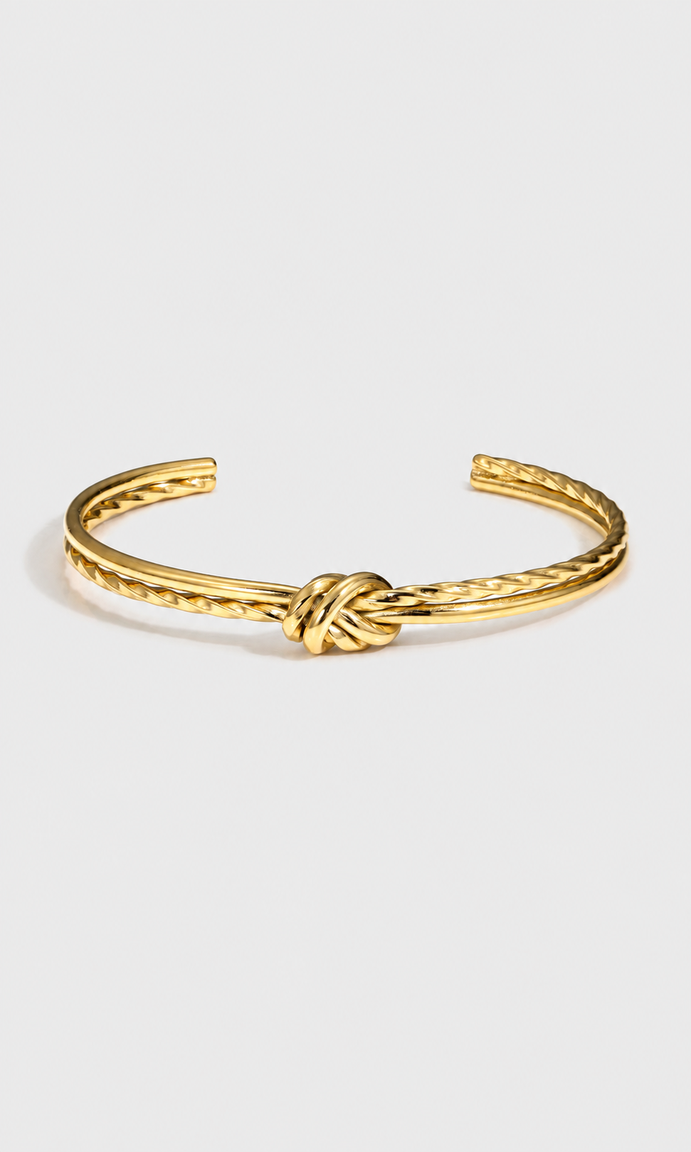 A gold-toned metal cuff bracelet featuring a textured twisted design and a central knotted detail, displayed on a clean light gray background.